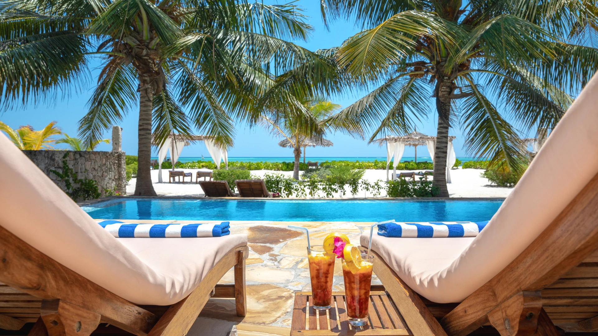 Poolside loungers beneath palms beside a tropical beach
